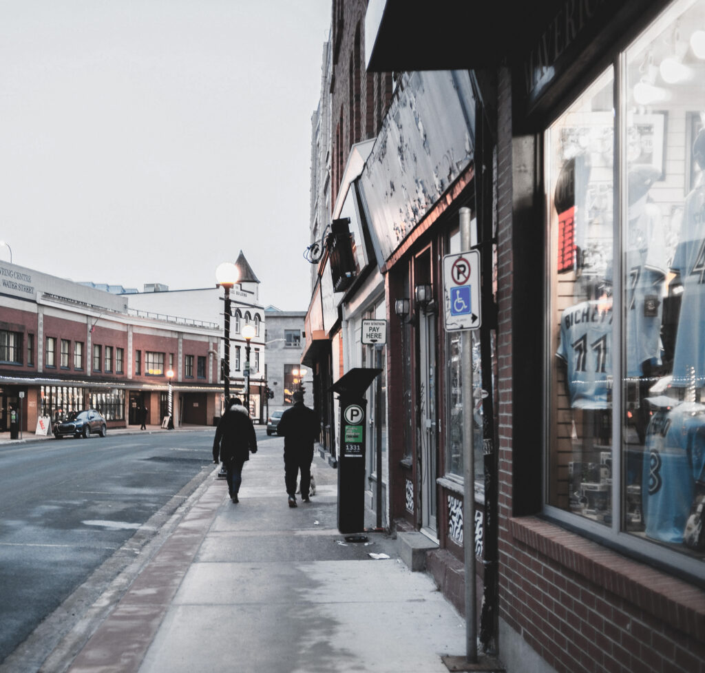 Photo by Eric Mclean | Pexels of two people wearing coats and hats walking away from camera on a sidewalk of main street in a small town