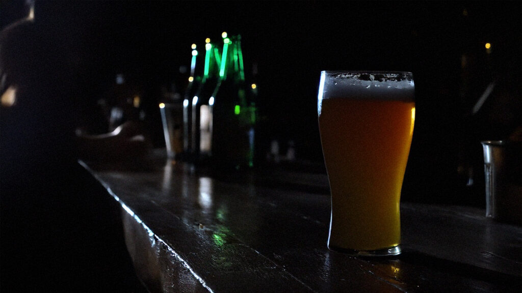 Photo of a single beer sitting on the bar of a dark dive bar.